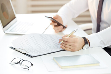 Close-up of unrecognizable manager in wristwatch sitting at office table and checking timetable in online calendar while working with papers in office