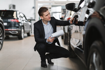 Handsome young sales manager making new automobile checkup at luxury car salon, full length