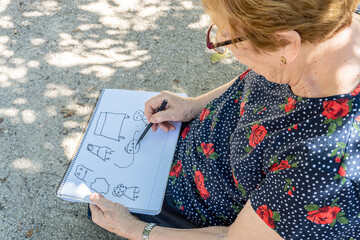 Hands of elderly woman with Alzheimer's, drawing doodles in a notebook. It is important to keep...