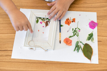 Faceless kid arranging pressed flowers onto a picture frame.