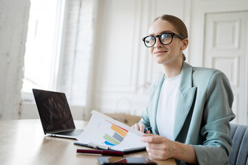 A woman with glasses for a computer freelancer works, uses a laptop, makes a report to a finance company