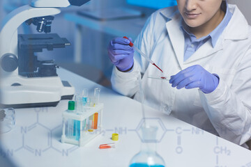 Close-up of concentrated lab technician sitting at desk and dropping blood on microscope slide while preparing sample for testing