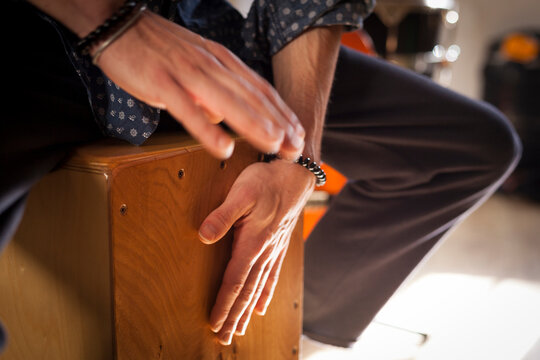 Detail of a percussionist male hands while playing flamenco drumbox on a rehearsal studio with drums and music stuff on the background with natural light. Flamenco instruments and musicology concept. 