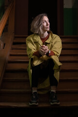 young caucasian pensive woman with short hair sitting alone at wooden staircase