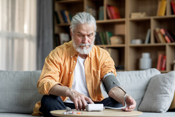Handsome senior man checking blood pressure at home - obrazy, fototapety, plakaty
