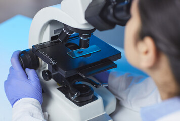 Over shoulder view of unrecognizable scientist investigating sample on glass slide via microscope...