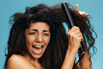 Screaming pretty Latin woman suffer with curly dry damaged hair problems using a hair straightener,...