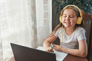 Speech training concept. Little girl uses a laptop and shows her teeth and smile to study at home with a teacher, a speech therapist. Distance learning.A kid doing exercises for correct pronunciation. - obrazy, fototapety, plakaty