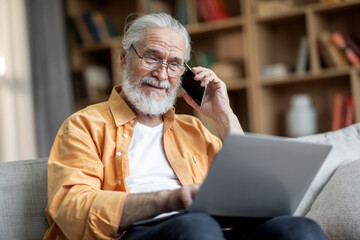 Positive handsome elderly man using laptop, having phone conversation