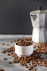 Roasted coffee beans in a white mug, coffee beans scattered around. 