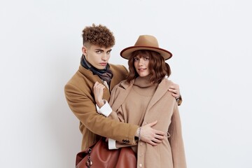 a sweet, joyful, pleasant stylish couple stands on a white background in autumn coats and gently hug each other, a woman has a hat on her head and she is holding a bag