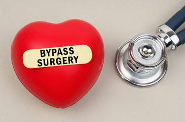 Near the stethoscope lies a heart on which a sticker is pasted with the inscription - Bypass Surgery - obrazy, fototapety, plakaty