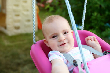 Fototapeta na wymiar Beautiful blonde smiling girl is swinging outside on a summer day.