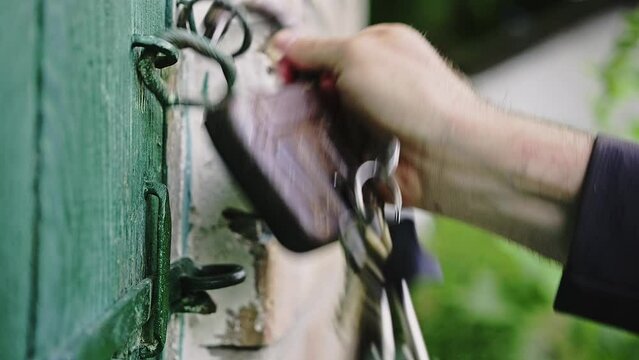 Close-up of a caucasian man's hand opens old padlock on the green wooden door