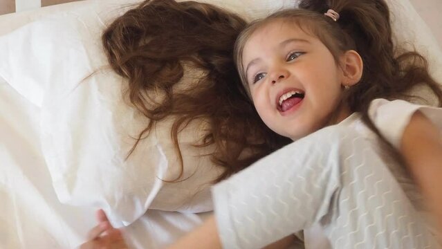 Before go to night or daytime sleep mother reading to daughter fairytale, kid enjoy storytelling lying with mommy in bed feels comfortable, good pastime develop reader skill, have fun at home concept