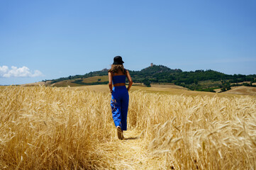 Naklejka na ściany i meble Girl walking through wheat fields in Tuscany