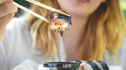 A young woman eating sushi in nature, maki roll close-up. © puhimec