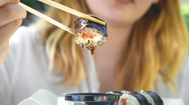 A Young Woman Eating Sushi In Nature, Maki Roll Close-up.