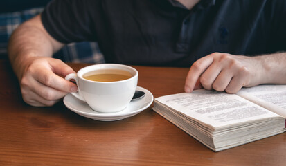 Close-up, a cup of tea and a book in male hands.