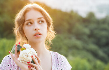 Close up portrait of a beautiful blonde with a white peony in her hands at sunset.