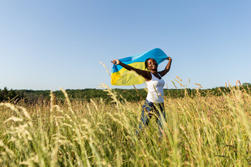 African american woman wrapped in ukrainian yellow blue flag flutters waving in the wind. National symbol of Ukraine. Stand with Ukraine, international support and solidarity
