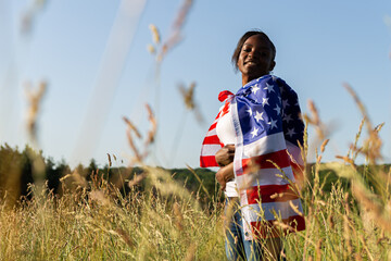 African american woman wrapped in american flag flutters waving in the wind. Happy 4th of July! Independence Day celebrating. Stars and stripes. Freedom concept.
