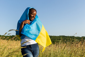African american woman wrapped in ukrainian yellow blue flag flutters waving in the wind. National...