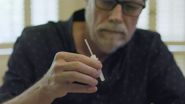 A senior adult male who has finished swabbing his nostrils placing the swab in the solution provided in the at home COVID-19 test kit.