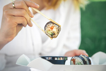 A young woman eating sushi in nature, maki roll close-up.