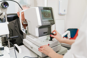 doctor examines elderly man's eye on screen of autorefractometer. 