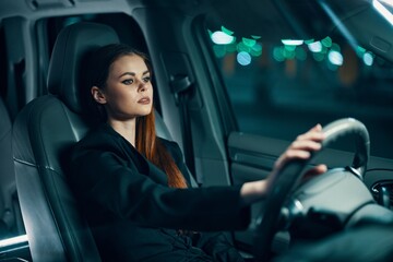 a horizontal photo from the side, at night, of a woman sitting behind the wheel in a black shirt, wearing a seat belt, looking at the road. Safe driving topics