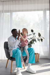 Side view A happy little preschool girl high-fives a male doctor at a hospital meeting