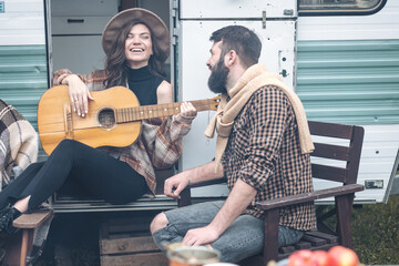 Young beautiful loving couple travelling across country in the van. Millennial man and woman in a travel camper. Cozy atmosphere, vacations vibe. Playing guitar, drinking tea, cooking on a campfire