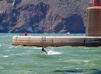 Brilliant kite surfing under the Golden Gate Bridge in Strong winds.  Surfer is shown against the concrete of the foundation. 