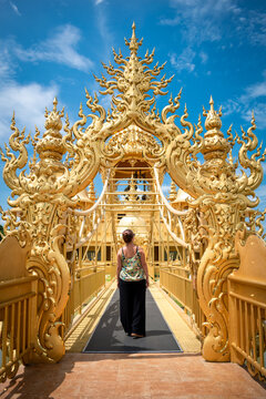 Mujer turista ingresando a templo budista, con puertas doradas