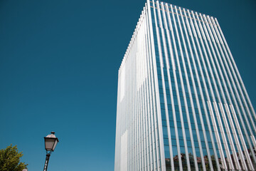 Obraz premium Modern tall multistory building steel and glass against blue dramatic sky. Office building view from bottom. Real estate investment. Mirrored windows facade in modern business quarter. Urban space.