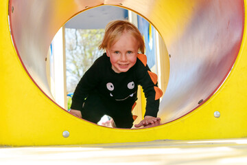 Cute funny blond little young toddler kid child boy crawling climbing through yellow plastic...