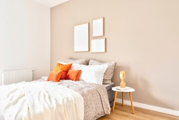 Fototapeta na wymiar Comfortable double bed with orange piloows, white bedding and blanket in cozy bedroom. Stylish interior in hotel with frame on the wall. Modern room in apartment at home. 