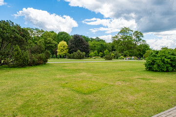Landscaping of a parking area with flowers and trees on a sunny day, an ennobled park area in a botanical garden with paths and green trees - obrazy, fototapety, plakaty