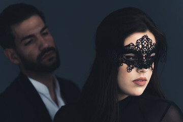 Attractive young european brunette woman in black outfit and a lacy carnival mask looking away....