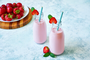 Strawberry smoothie or milkshake in glass jar with berries on blue concrete background.