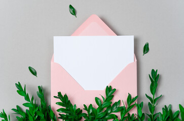 Real photo. Pink envelope square invitation white greeting card mockup with a boxwood branch. Top view with copy space, pastel grey background. Template for branding and advertising
