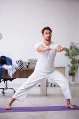 Fototapeta premium Young male employee doing sport exercises in the office