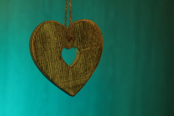 Grey wooden heart suspended by string against a green background