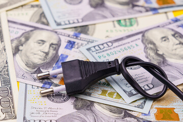 Plug from an electric cord tied in a knot on a blurred background of dollars, selective focus
