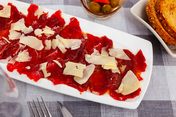 Raw beef meat, carpaccio, served on plate and topped with pieces of cheese.