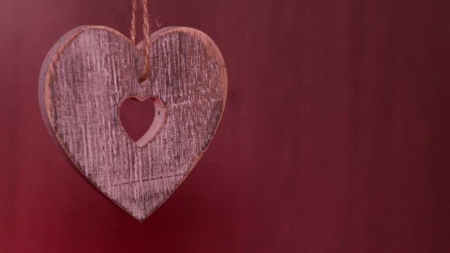 Wooden heart suspended by string against reddish-brown background