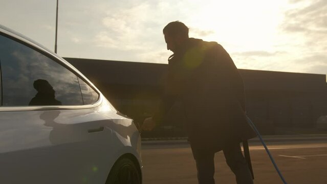 Businessman browsing on a smartphone while waiting to charge his electric car at a charging station in an airport