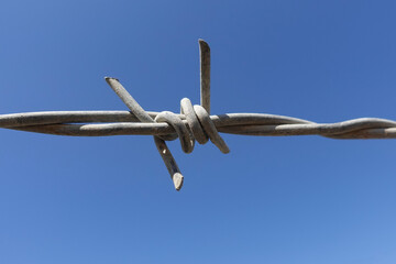 CLose up of barbed wire barb against blue sky.