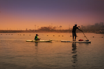 father and son surfer rides  by paddle board (S.U.P.) in the ocean against the background of costa verde (lima,peru) on sunset